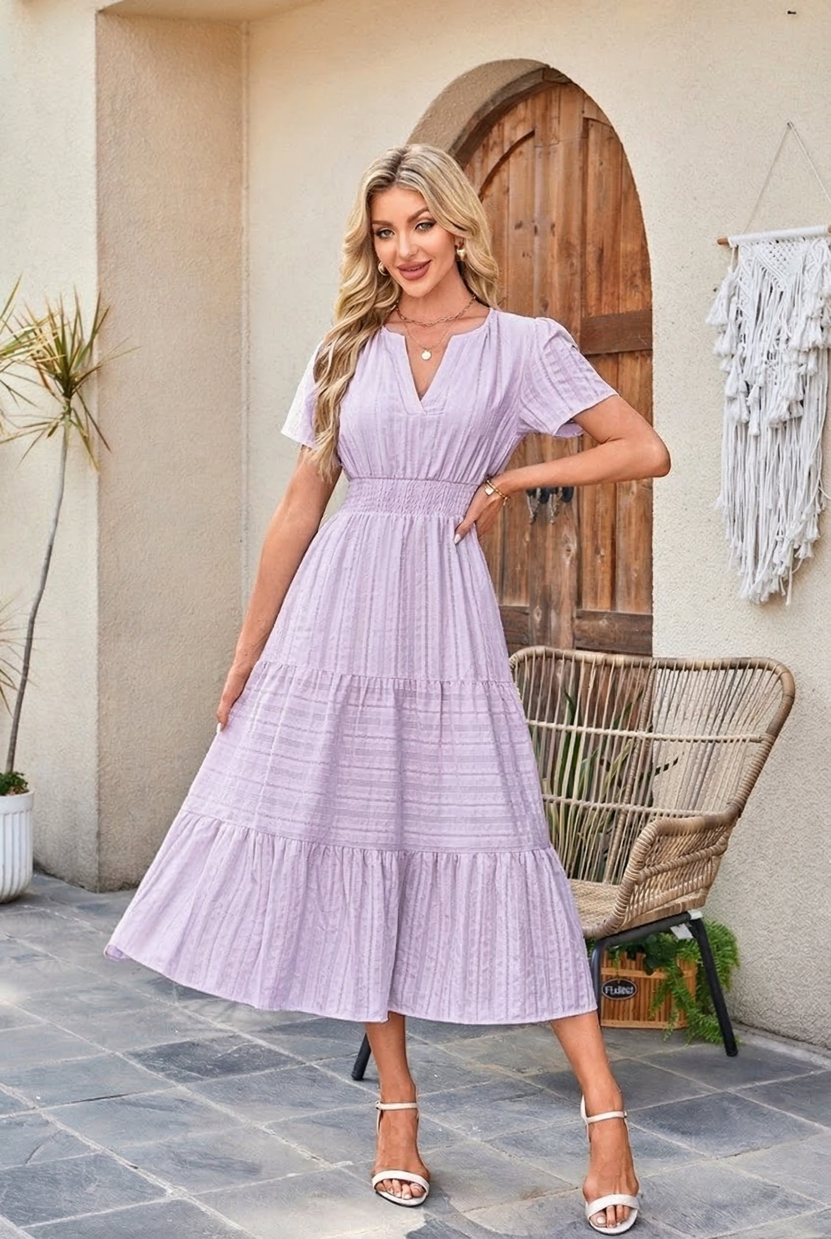 Woman wearing a light purple dress standing in front of a wooden door.